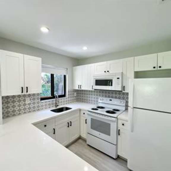 a white kitchen with a refrigerator, stove, and microwave.
