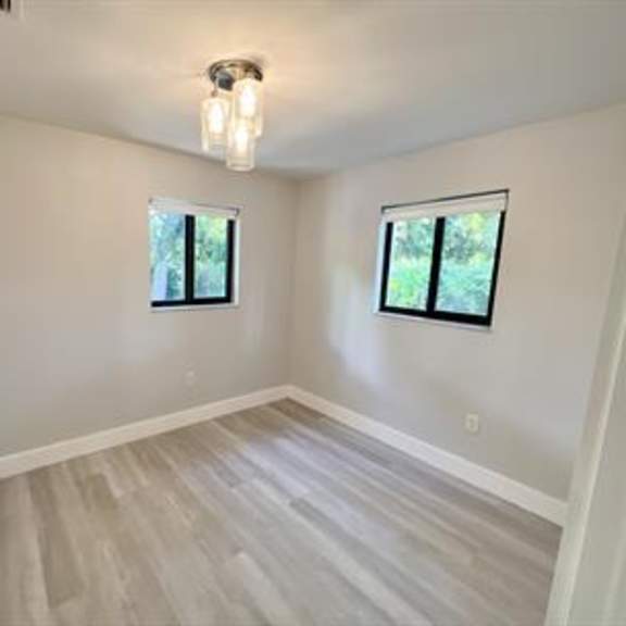a room with light wood flooring and two windows.