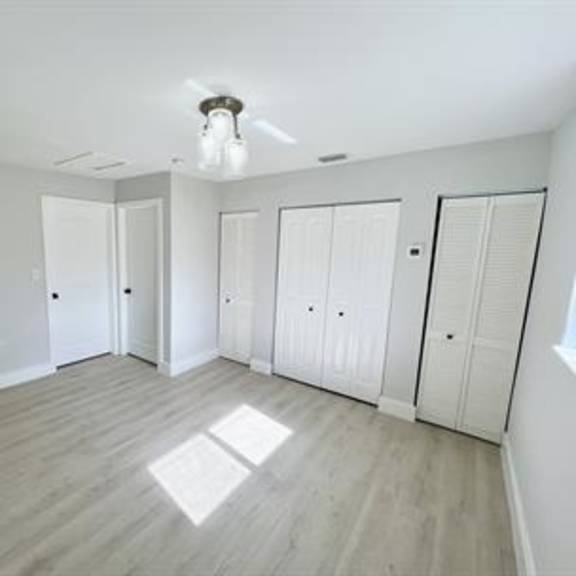 a room with white walls and a light wood floor with a ceiling fan and a window letting in light.