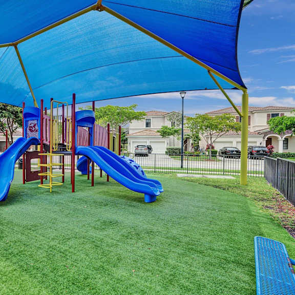 gate enclosed, covered playground with a blue slide and a green canopy.