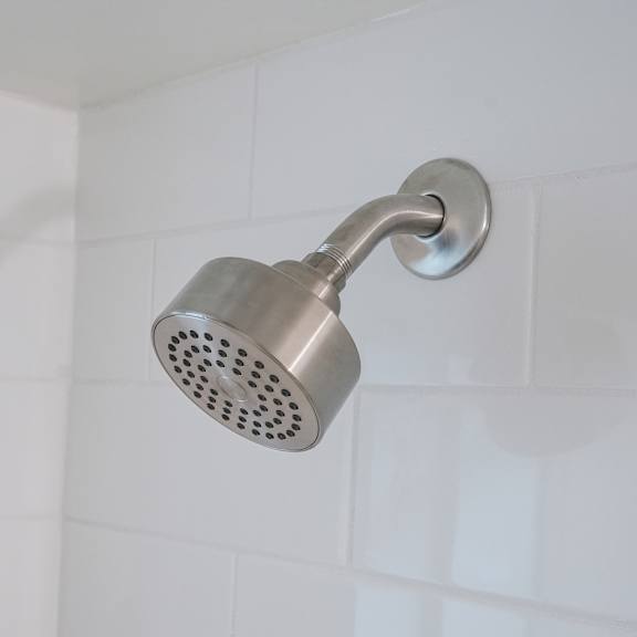 a shower head mounted on a white tiled wall.