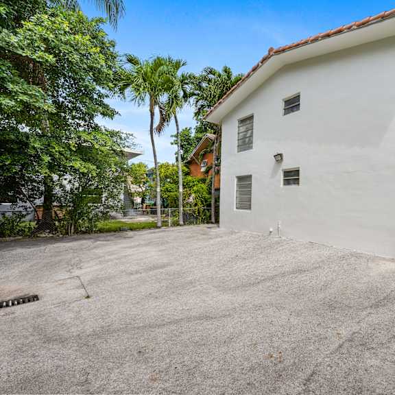 a white building with a red roof is surrounded by trees and has a concrete driveway in front.