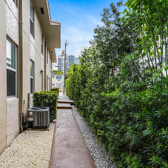 a narrow pathway leads between two buildings with a green hedge on the right.