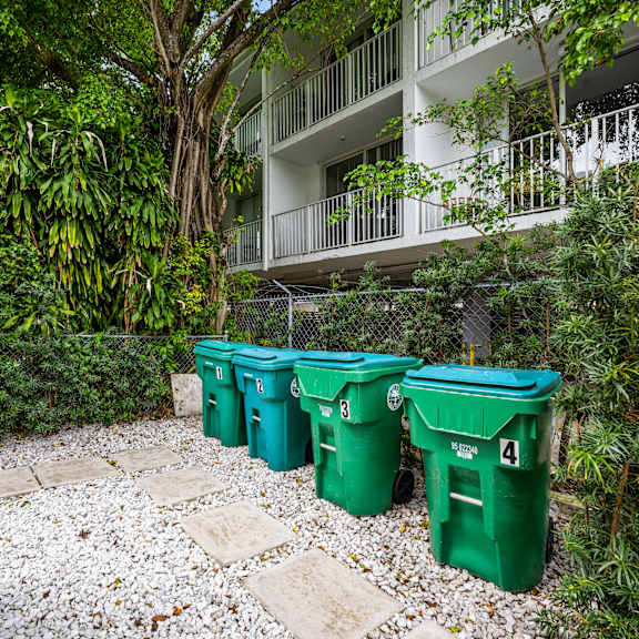 four green bins are lined up in a garden.