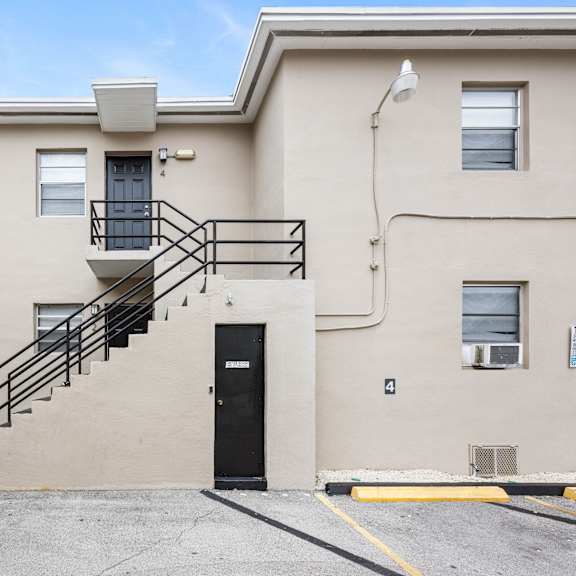 a beige building with a black door and a staircase leading to the second floor.