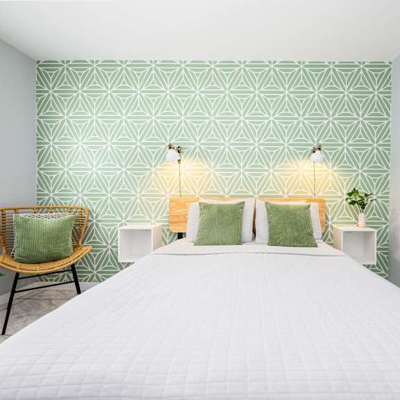 a bedroom with a white bed and green patterned wallpaper.