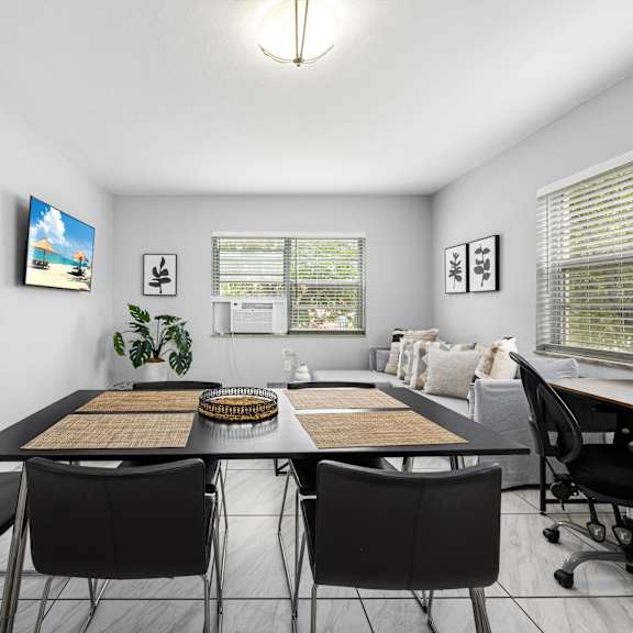 a room with a table and chairs in the foreground and a painting of a beach scene on the wall.