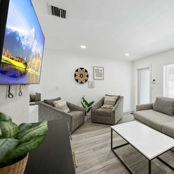 a living room with a grey couch, a white coffee table, and a tv on the wall.
