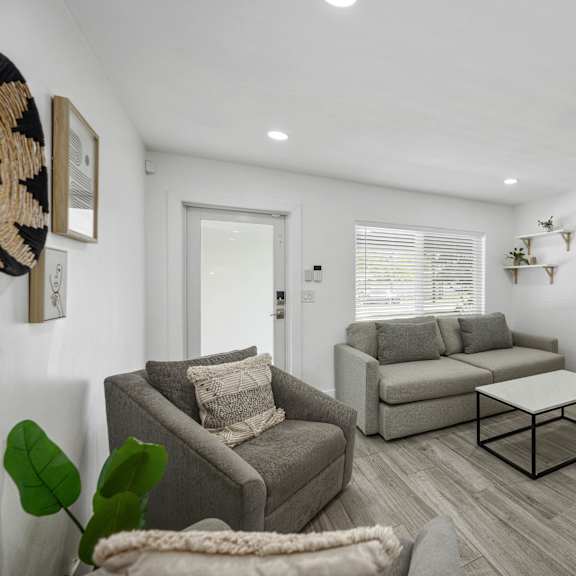 a living room with a grey couch, a grey armchair, a white cabinet, and a white framed picture on the wall.