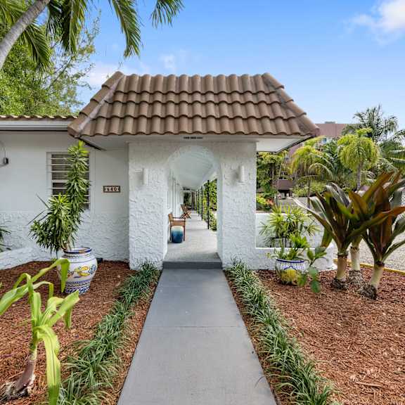 a white house with a red tile roof and a concrete pathway leading to the entrance.
