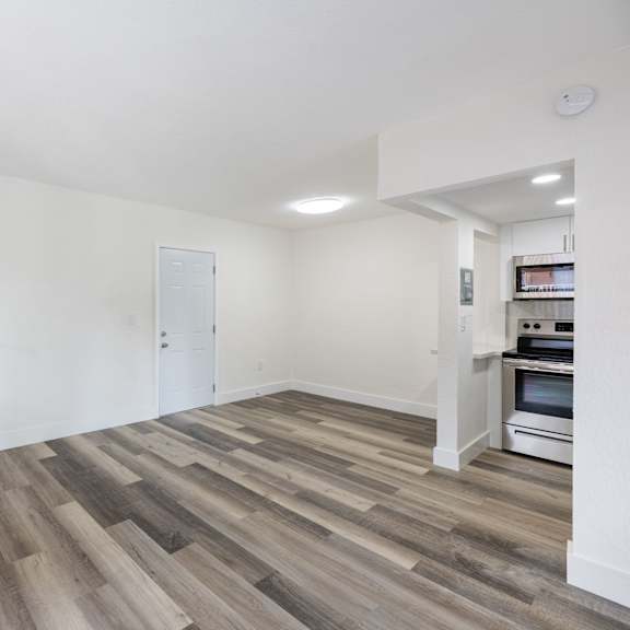 a room with a wood floor and a kitchen in the background.