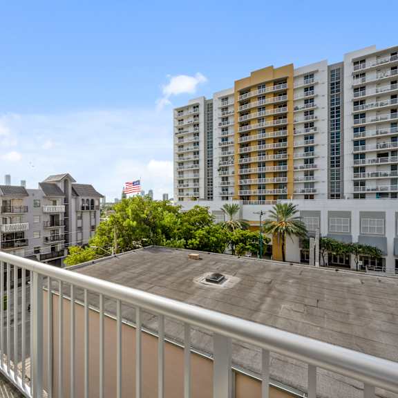 a balcony with a metal railing overlooks a cityscape with buildings and palm trees.