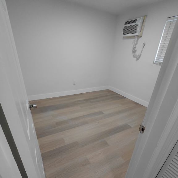 a room with a wooden floor and a white wall with a window.