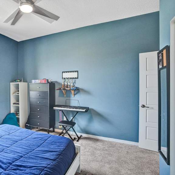 a bedroom with a bed, a window, a fan, and a desk with a chair.