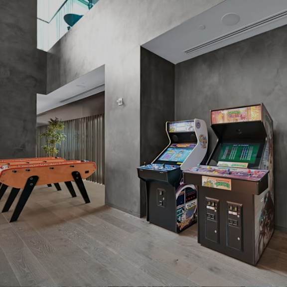 a room with a table, a sofa and three arcade games.