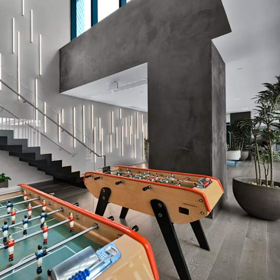 a foosball table is in the middle of a room with a staircase and potted plants.