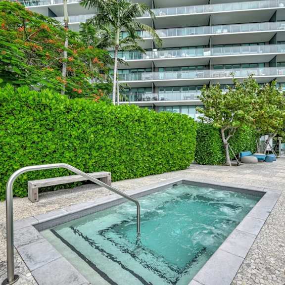a small pool surrounded by a stone walkway and greenery.
