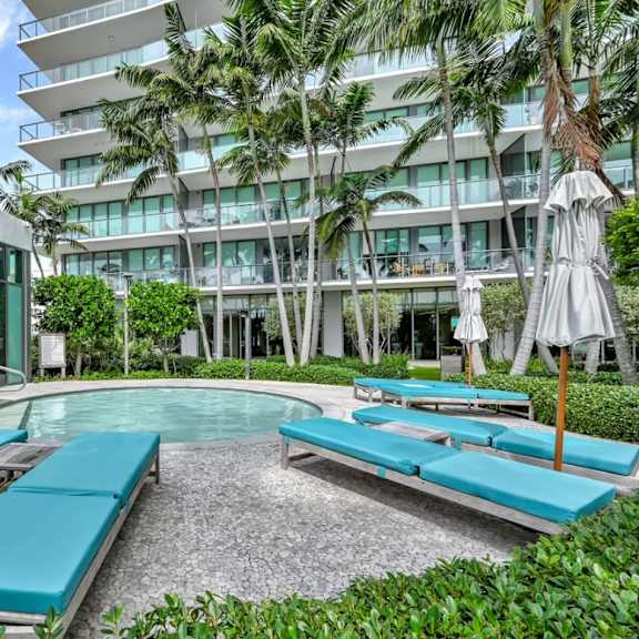 a pool area with sun loungers and umbrellas in front of a modern building.