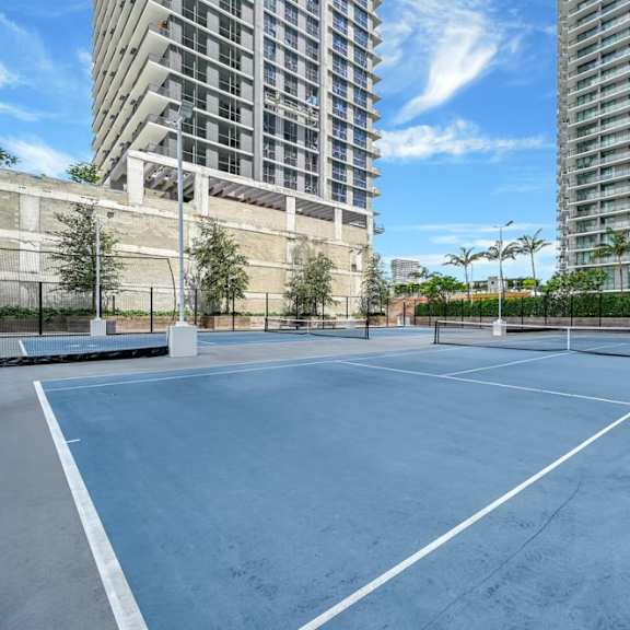 a tennis court surrounded by tall buildings and trees.