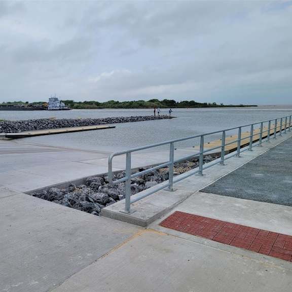 a walkway with a yellow post and a red brick patterned area leading to a body of water with a boat in the distance.