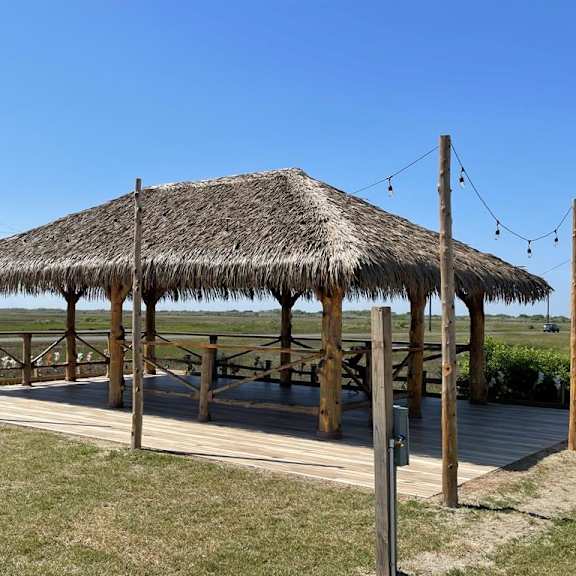 a thatched pavilion with a wooden deck and a bench.