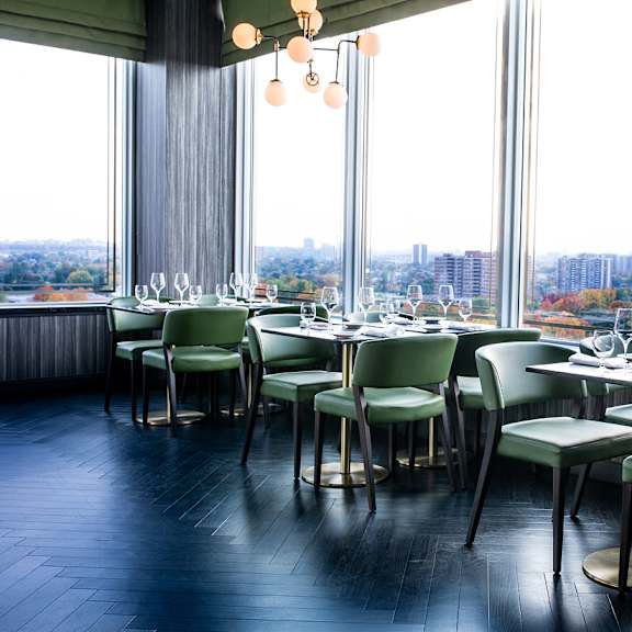 a restaurant with green chairs and tables set for dining with a view of the city.