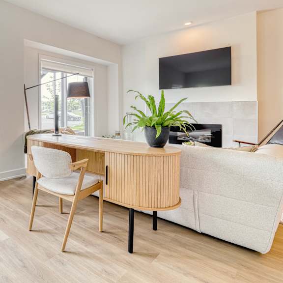 a living room with a grey armchair, a wooden chair, a white sofa, and a tv mounted on the wall.