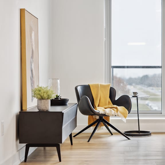 a black chair with a yellow throw is in front of a large window at the dale apartments , ontario