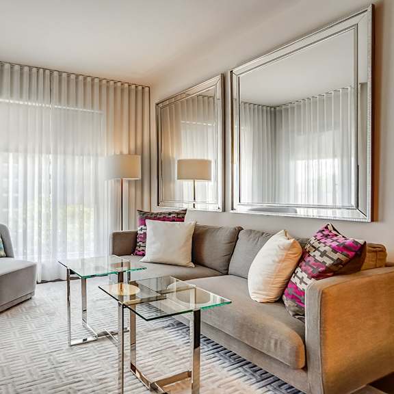 a modern living room with a grey couch, a glass coffee table, and a large mirror.