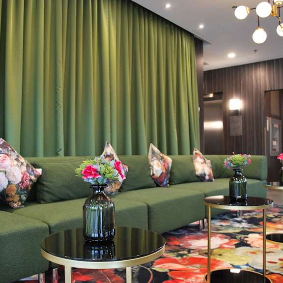 a green couch with floral pillows and vases on it.