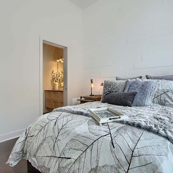 a bed with a leaf patterned comforter is in the foreground of a room with a lamp on the side.
