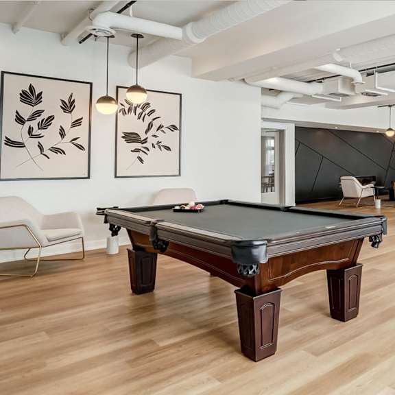 a pool table is in the middle of a room with a chair and a painting on the wall.