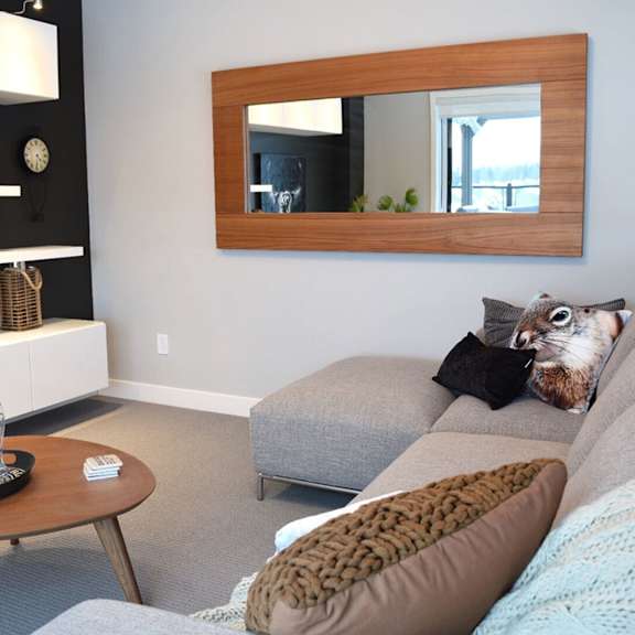 a living room with a grey couch, a brown pillow, a wooden coffee table and a mirror on the wall.