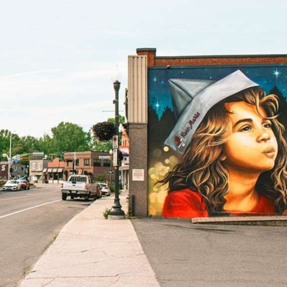 a large mural of a woman wearing a hat is on the side of a building.