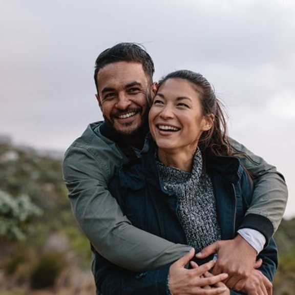 a man and a woman are embracing each other in a natural outdoor setting.