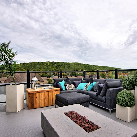 a modern outdoor patio with a black couch, wooden table, and concrete planters.