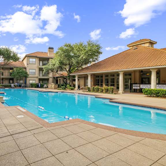 a swimming pool surrounded by a tiled patio and buildings.