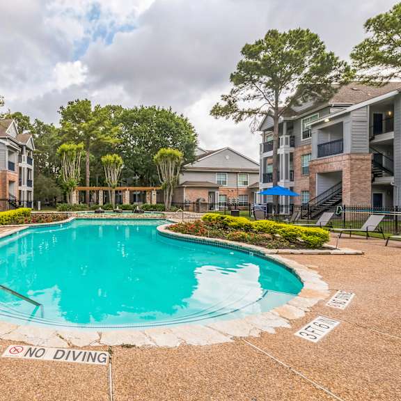 a pool surrounded by apartment buildings and tall trees.