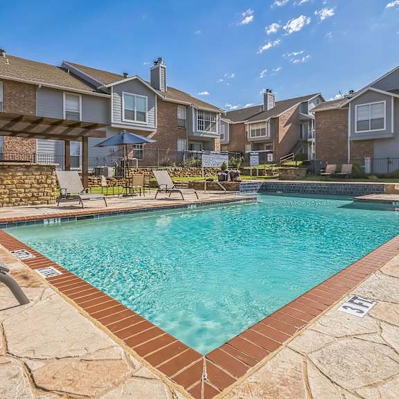 a swimming pool surrounded by a stone border and lounge chairs.