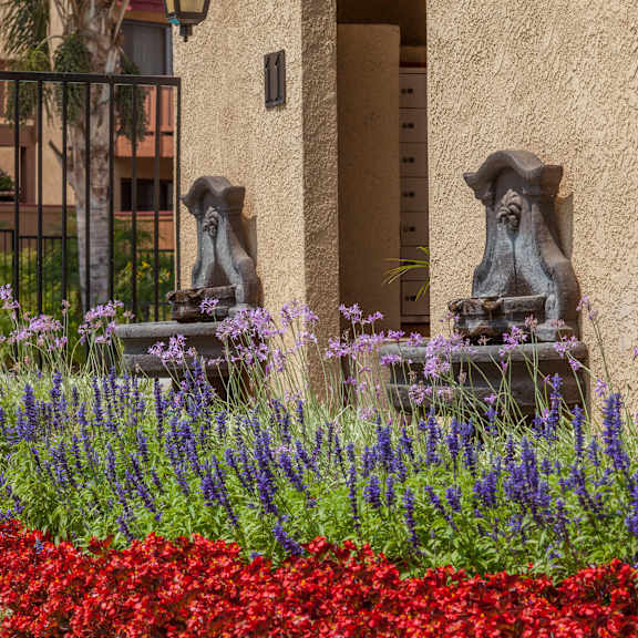 a garden with red flowers in the foreground and two stone lions in front of a building.