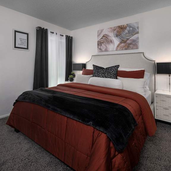 a bedroom with a red comforter and a white nightstand.