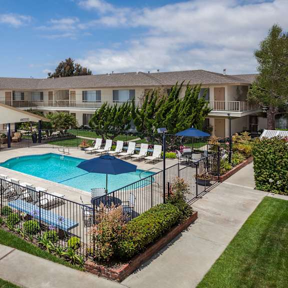 a swimming pool surrounded by a fence and umbrellas in a residential area.
