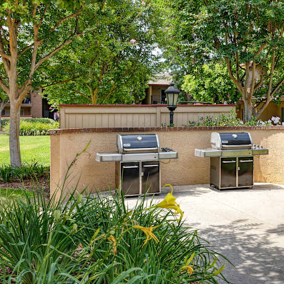 two bbq grills are situated on a concrete platform in a grassy area.