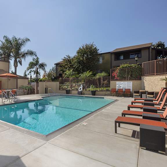 a pool surrounded by chairs and umbrellas with a building in the background.