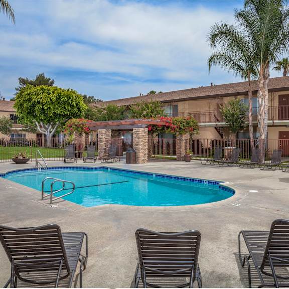 a pool surrounded by chairs and plants with a building in the background.