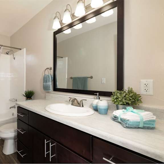 a bathroom with a dark brown cabinets and a wide mirror.