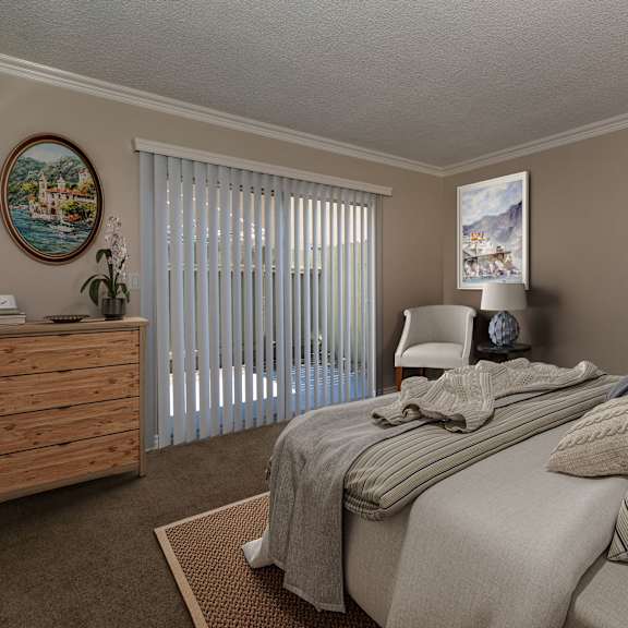 a bedroom with a bed, pillows, a nightstand, a plant, and a window with blinds.