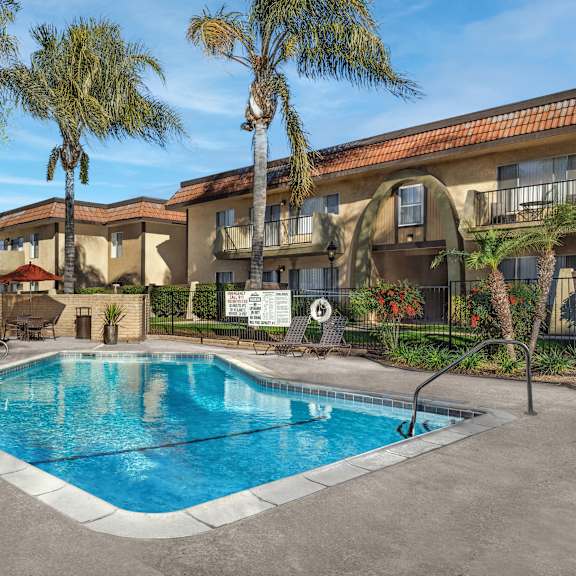 a pool surrounded by palm trees and a building in the background.