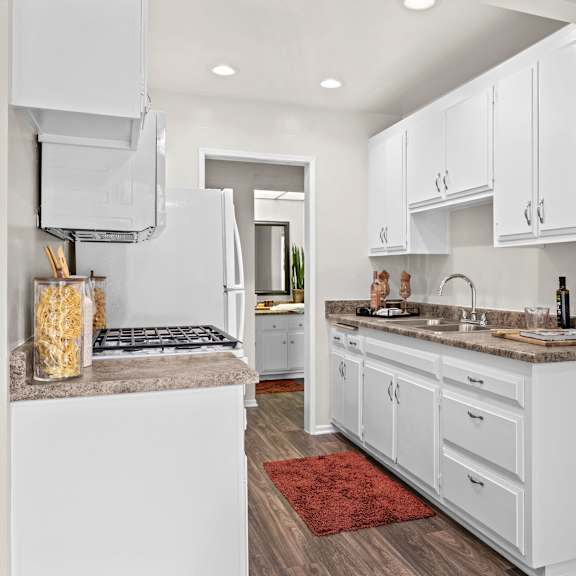 a kitchen with white cabinets and a red rug on the floor.