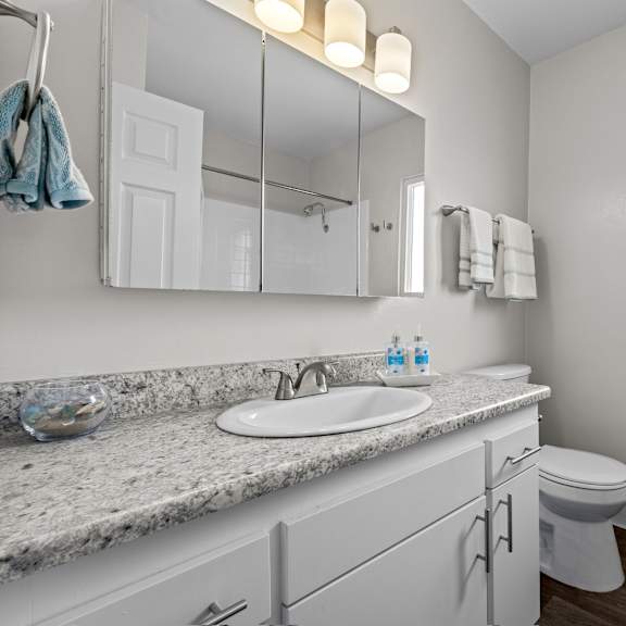 a bathroom with a sink, mirror, toilet, and a window.